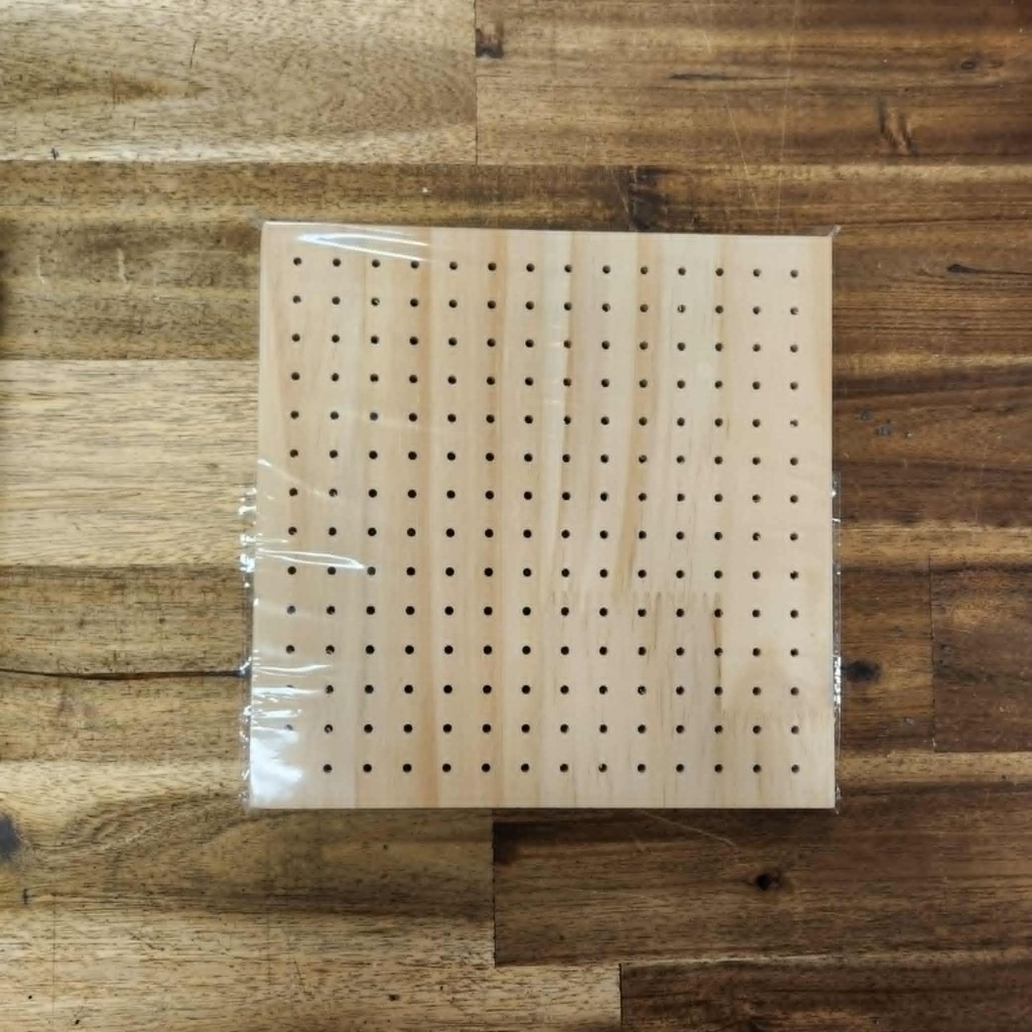 A square-shaped bamboo crochet blocking board with visible holes for pinning, placed on a wooden surface.